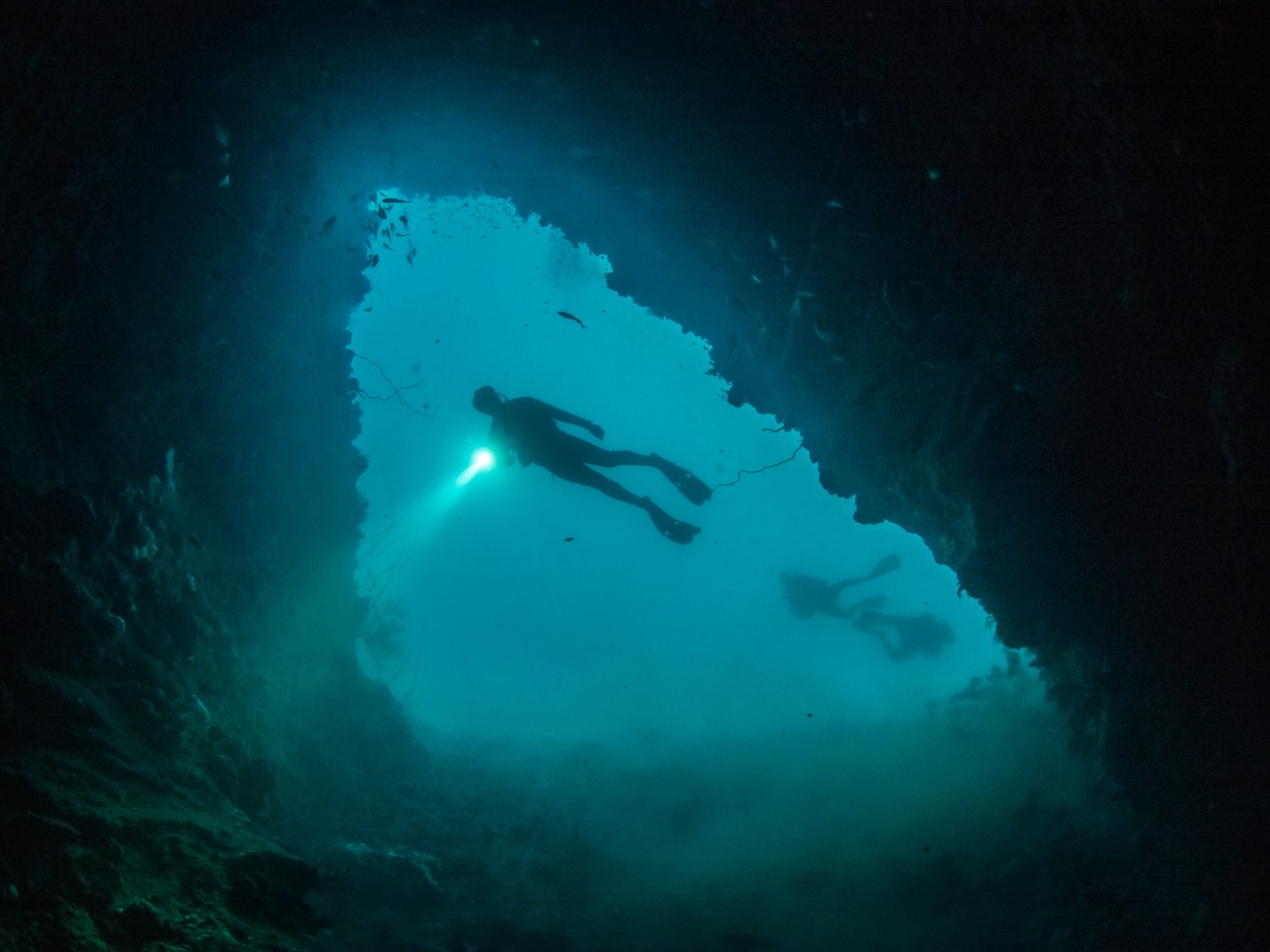 Cave Diving in Thailand - a cave diver starts to enter a cave from the open water. He or she is carrying a torch.