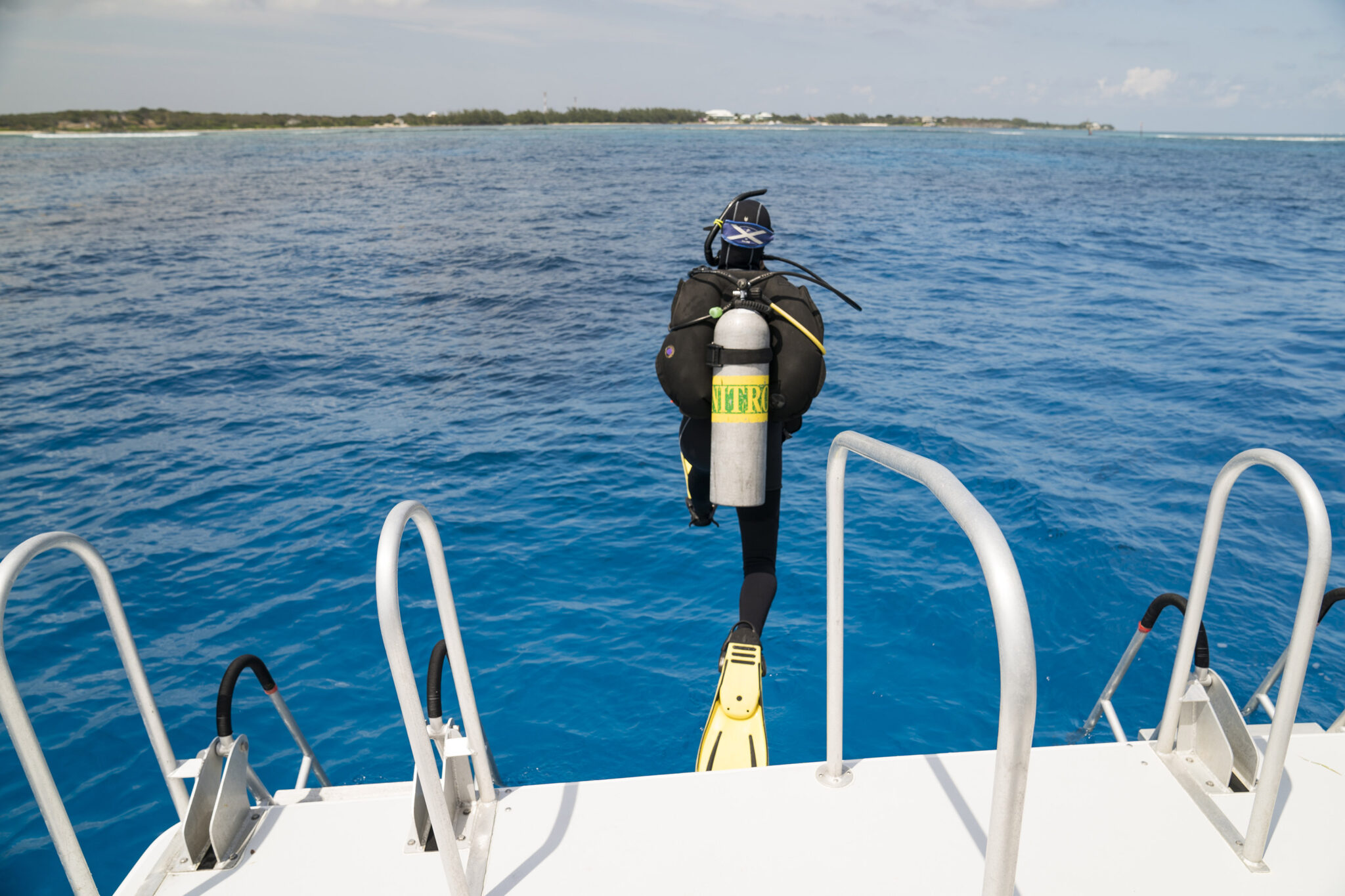 A scuba diver jumping into the ocean from the back of a dive boat and who is using a tank filled with enriched air nitrox