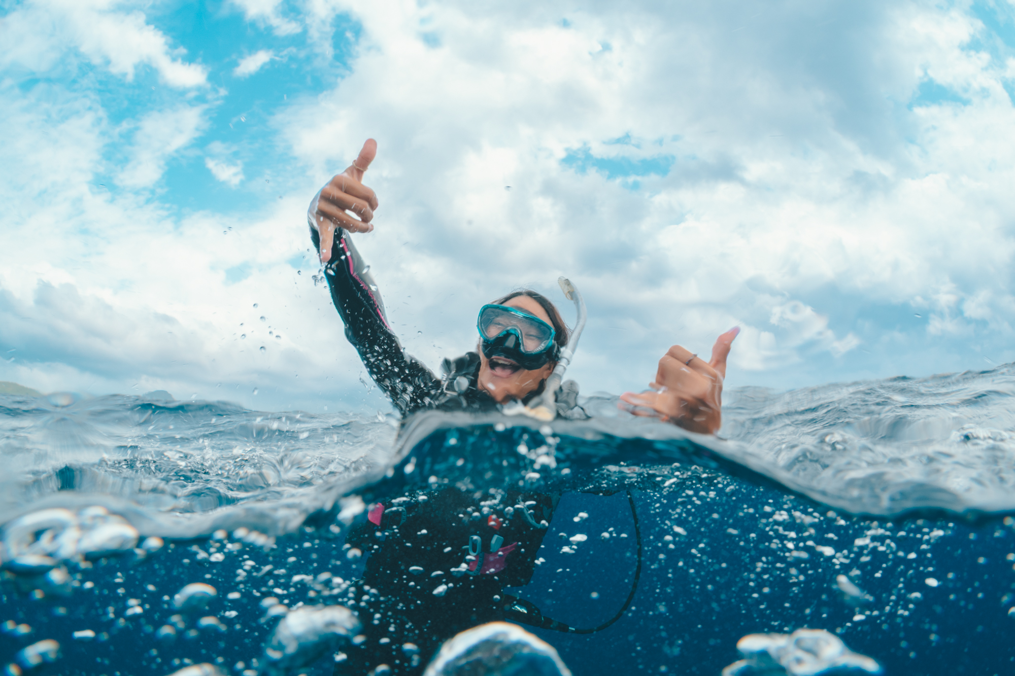 A diver celebrates at the surface with two shakas after a great dive