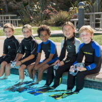 A group of kids sitting on the edge of a pool waiting for a scuba diving lesson