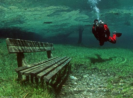 A diver hovers in a lake, over a submerged park bench