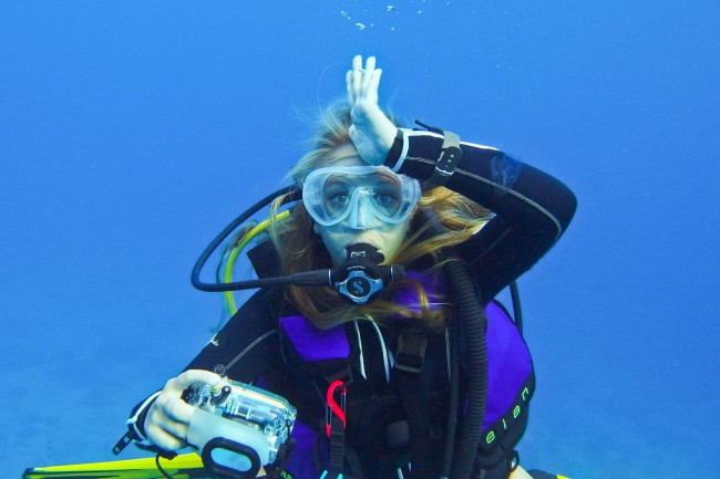 PADI AmbassaDiver Alex Baackes holding a camera and doing the shark sign, one of many diving hand signals for marine life
