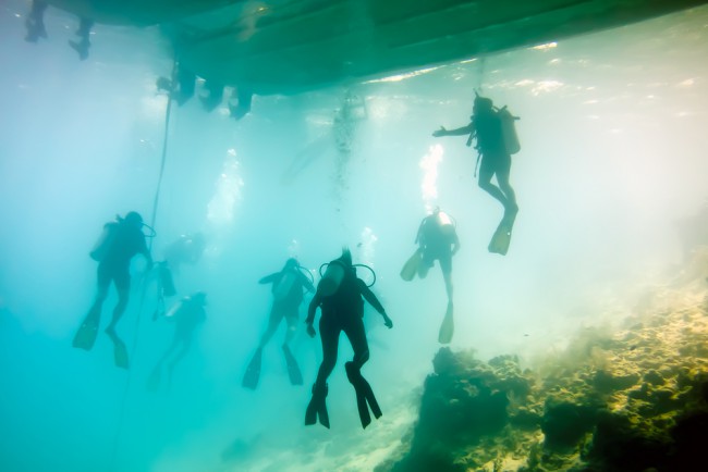 scuba divers under a dive boat over a shallow reef