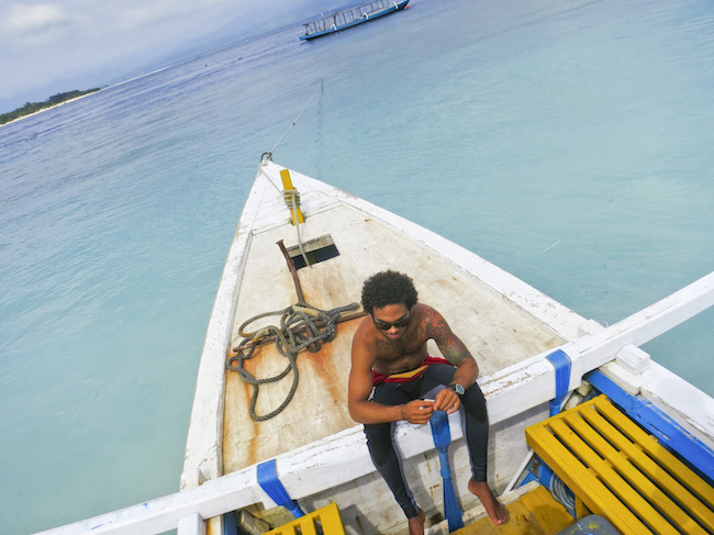 a man sits on a beam of a boat in a wetsuit in Indonesia