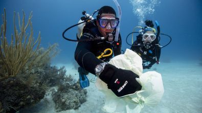 Two divers picking up rubbish underwater, one holds a plastic bag