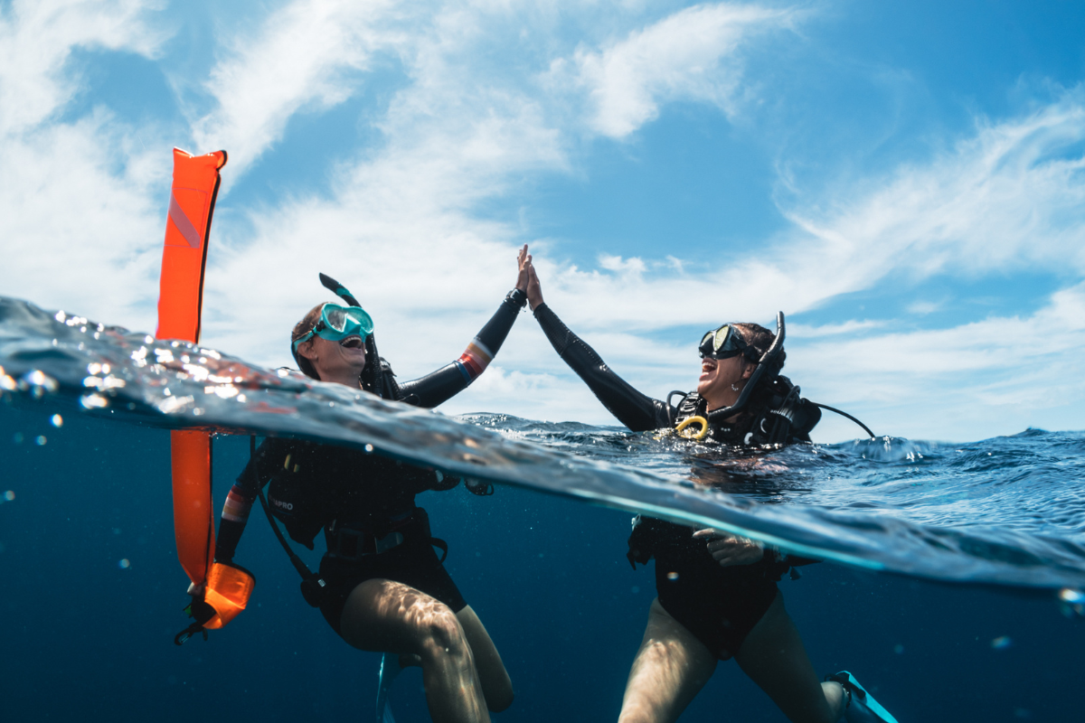 Twee duikvrienden geven elkaar een high five aan het wateroppervlak.