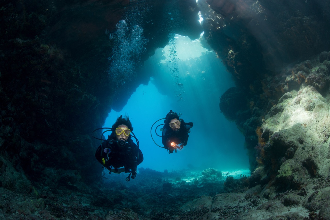 Two PADI Advanced Open Water Divers swimming through an underwater cavern who have no questions about liveaboard diving