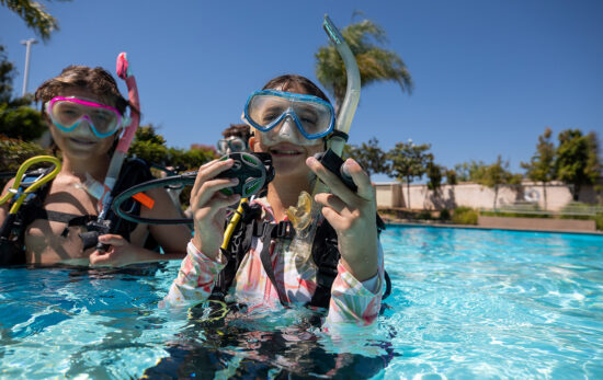 a young scuba diver adjusts her gear in a swimming pool