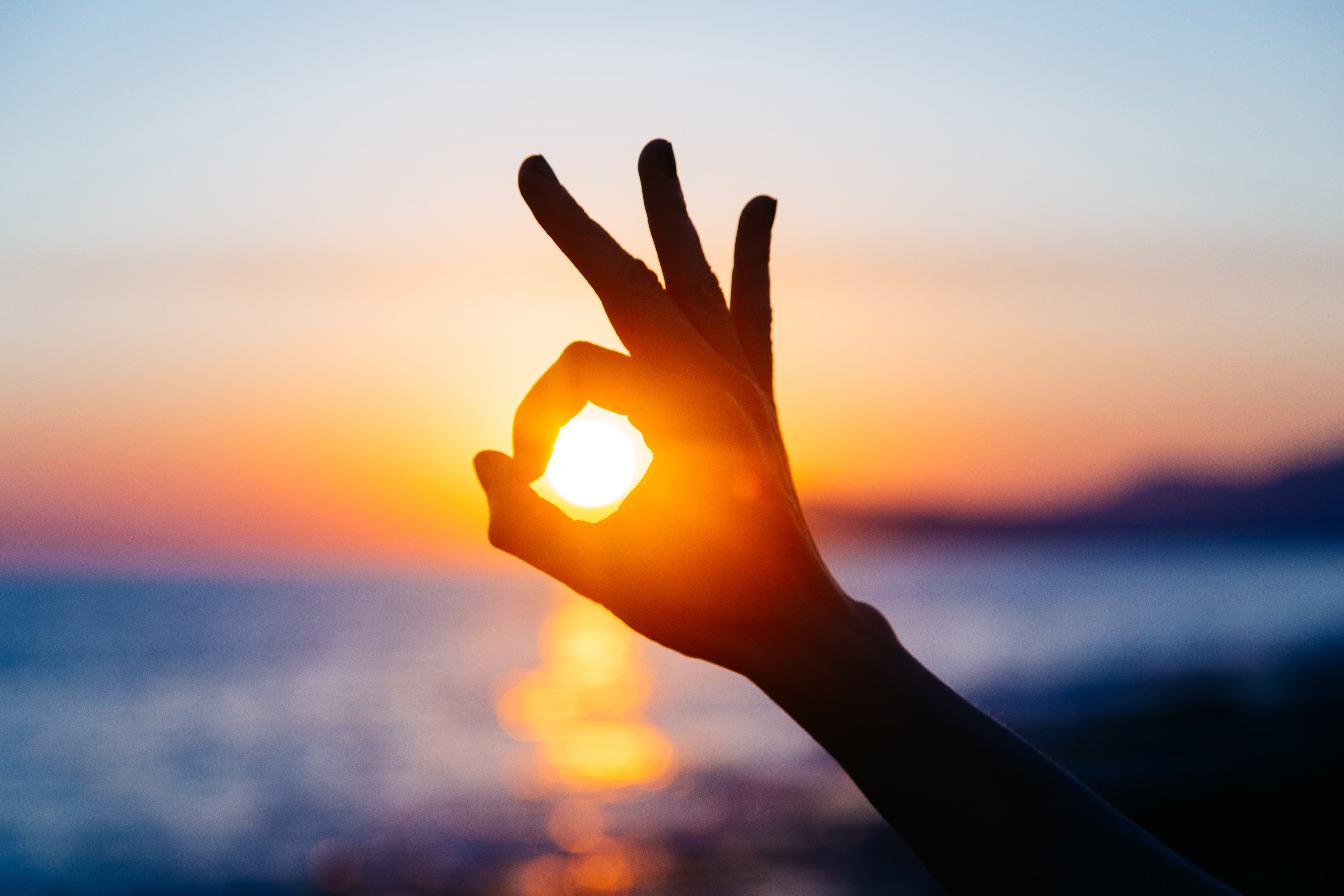 Hand giving the ok sign with sun setting in the middle of the ok.