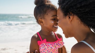 Mother embracing daughter with sunscreen on face at beach.