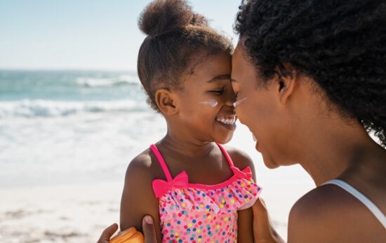 Mother embracing daughter with sunscreen on face at beach.