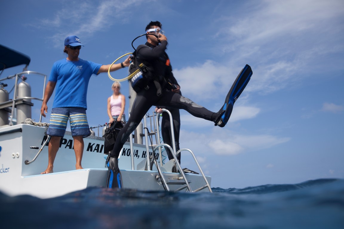 A diver making a giant stride entry into the ocean, where submersion in colder water will make them want to pee more often