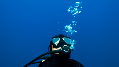 Scuba diver looking at scuba bubbles caused from exhaling underwater.
