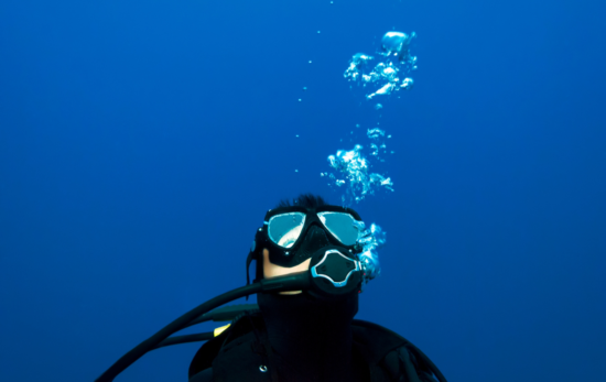 Scuba diver looking at scuba bubbles caused from exhaling underwater.