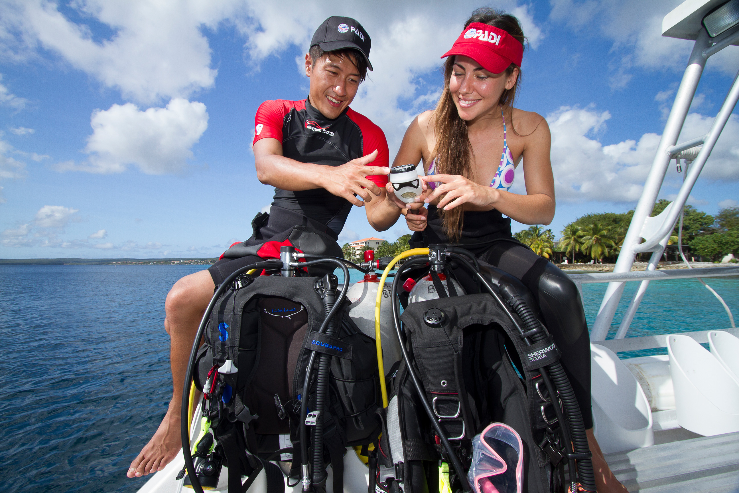 A PADI Instructor shows a student how to check their scuba gear, which is part of the full PADI Open Water Diver course