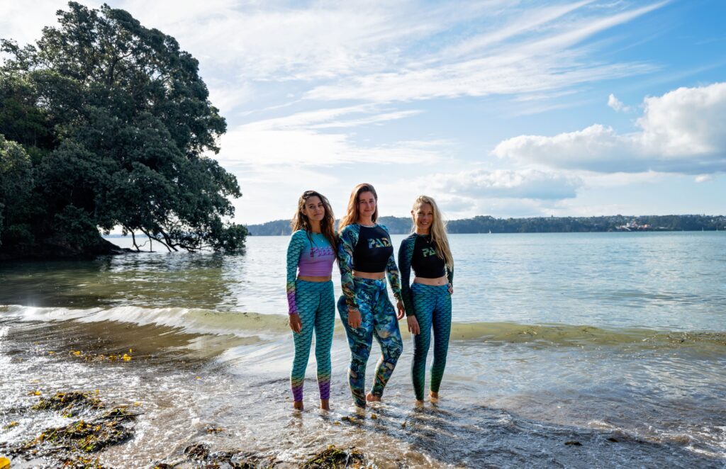 padi gear mermaid collection - three women stand on the seashore wearing cape cali leggings and padi rashguards