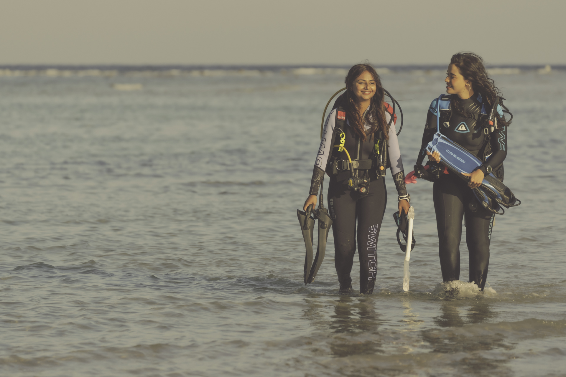 two female divers emerge from the ocean in Egypt carrying their masks and fins