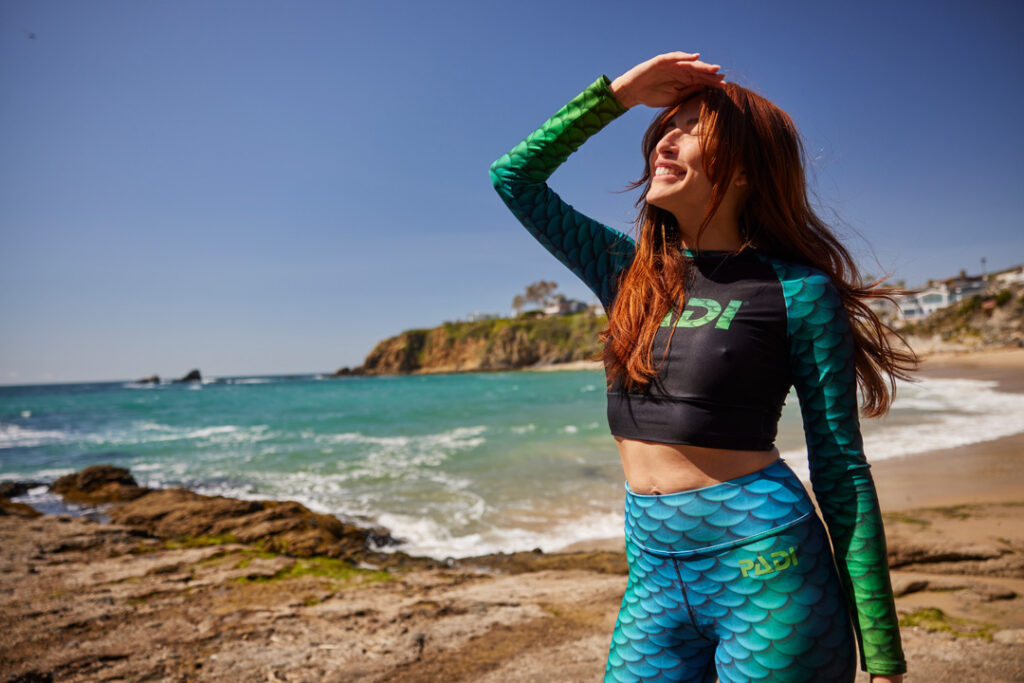 padi gear mermaid collection - a woman shields her eyes on the seashore wearing cape cali leggings and padi rashguards