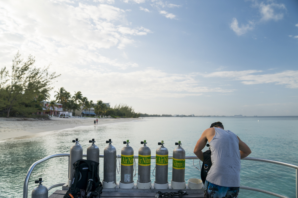 A PADI Enriched Air Diver prepares his nitrox diving equipment next to a line of scuba tanks on a dive boat near the shore
