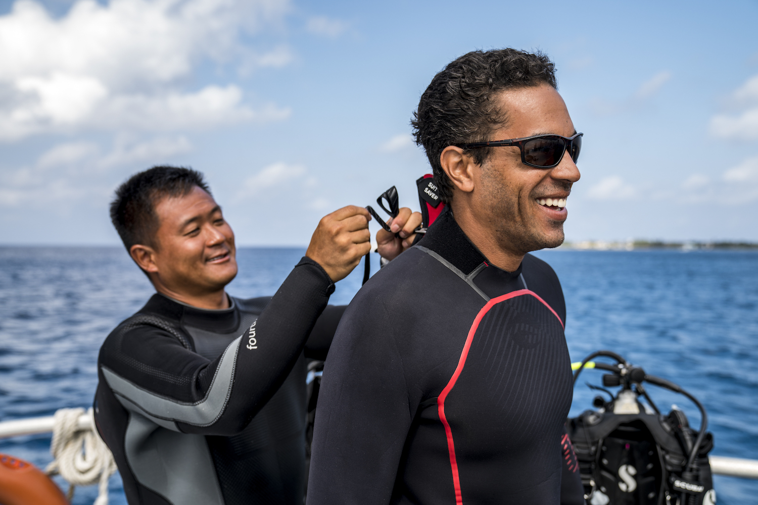 A scuba diver helping his buddy put on his wetsuit, a useful distraction for a way how to get over anxiety when scuba diving
