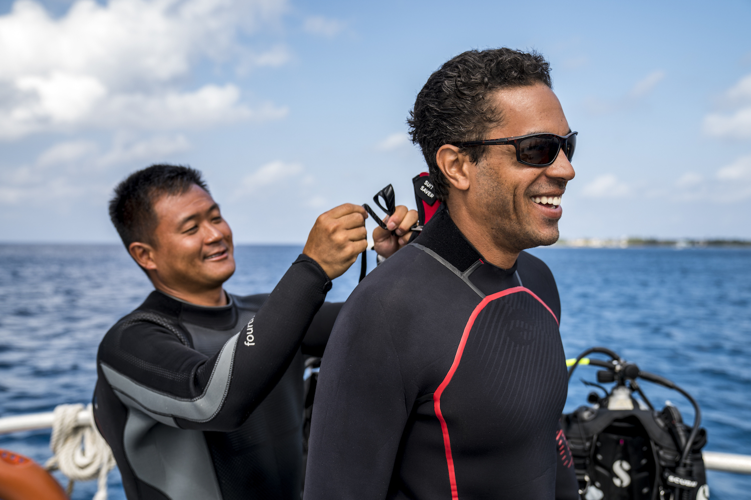 A diver helping to zip up his buddy's wetsuit before a scuba dive