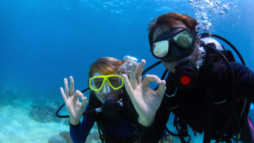 Two divers giving the OK sign underwater, a hand signal that you might like to see after using one of your best pickup lines