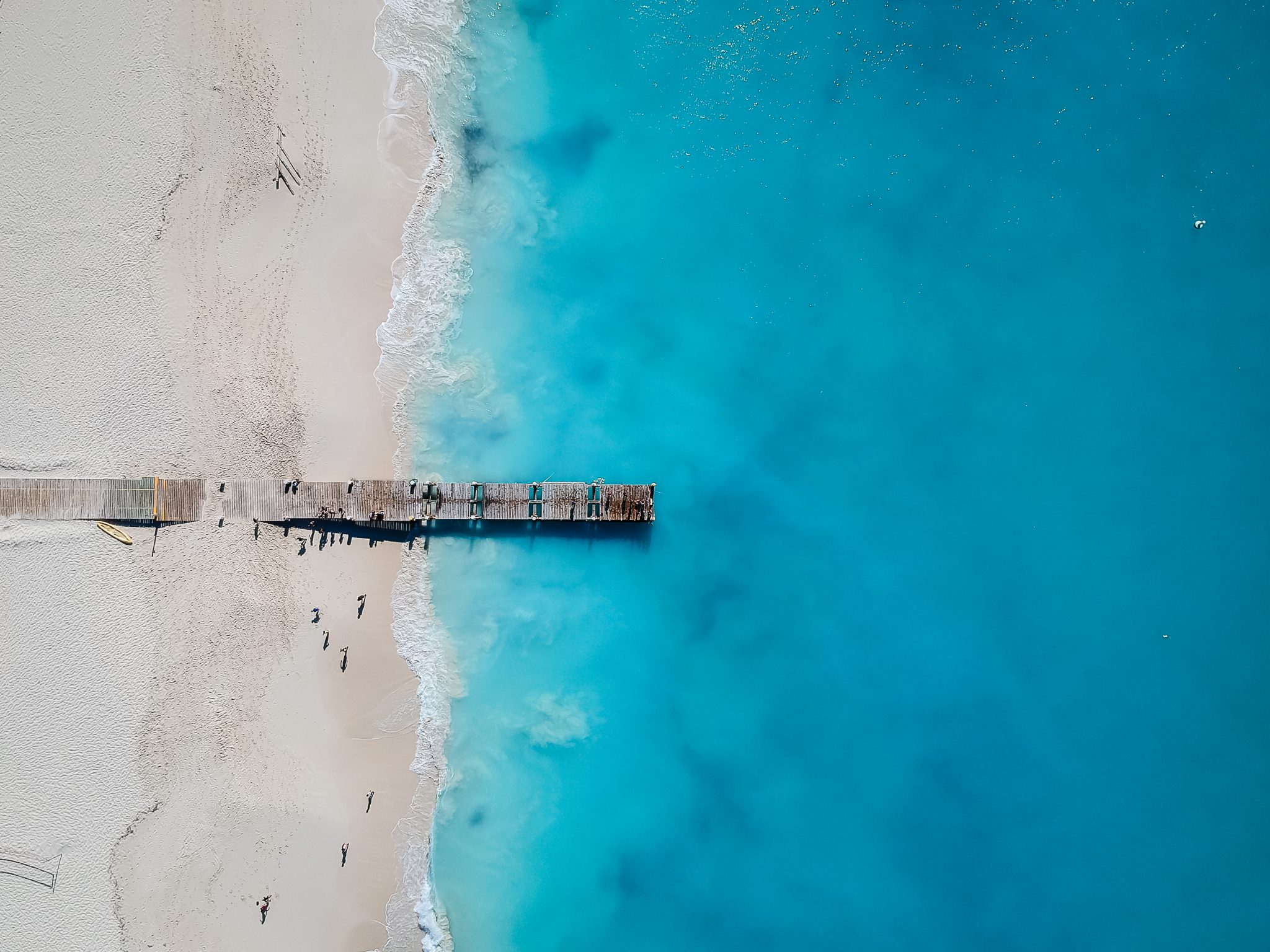 An aerial view of a jetty extending from white sands into clear blue water in Turks and Caicos, a top Caribbean destination