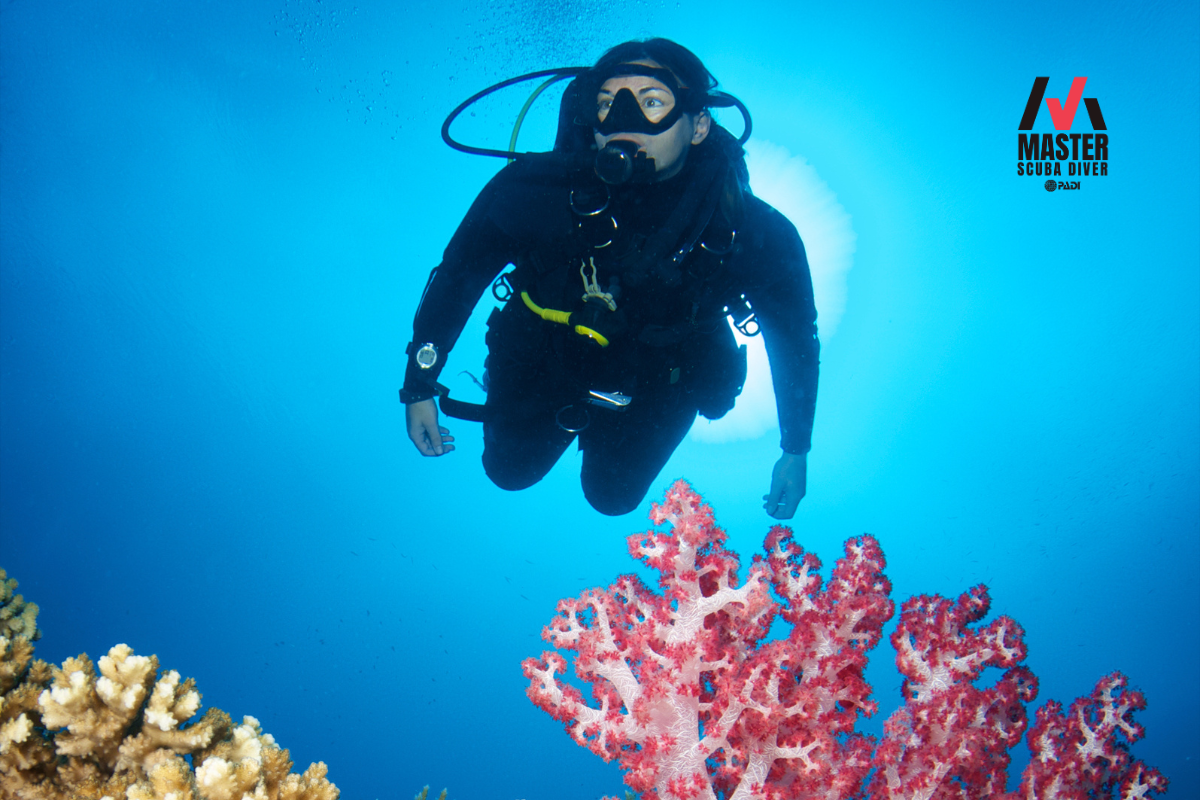 Scuba diver exploring a coral reef with a display of the Master Scuba Diver logo.