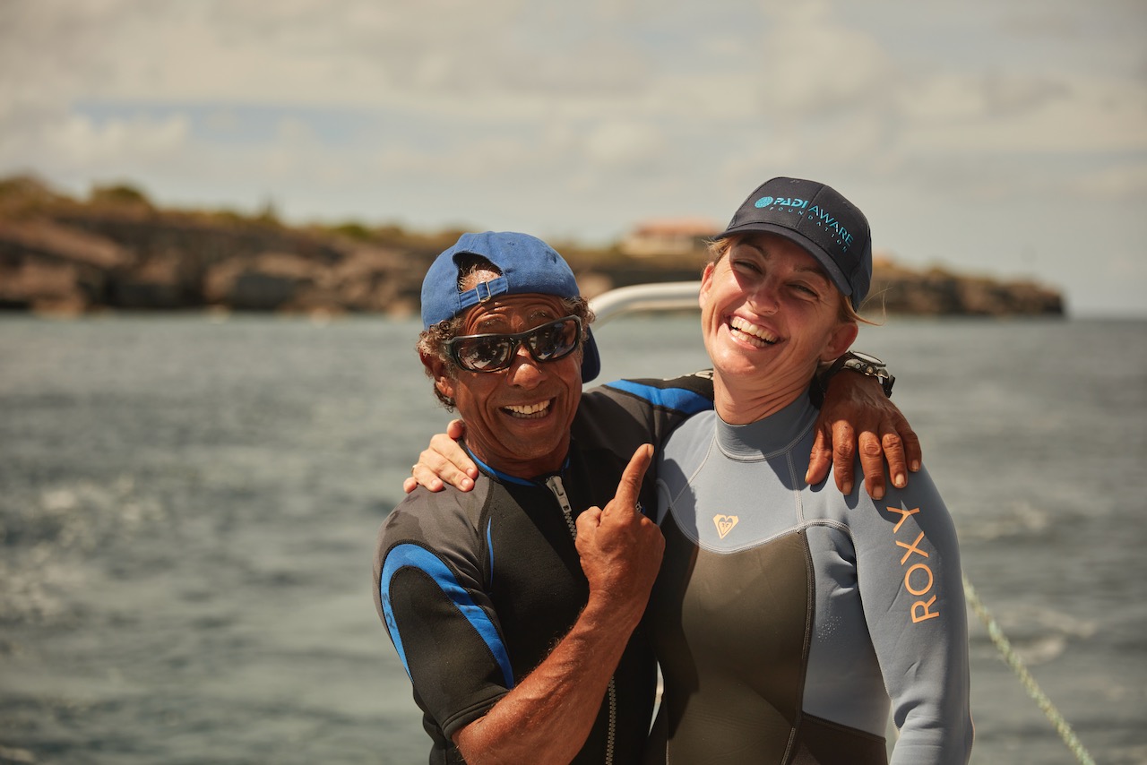 Two PADI instructors hug each other like friends near the shoreline
