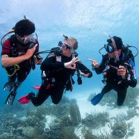 three divers underwater use hand signals