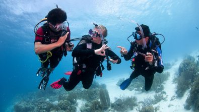three divers underwater use hand signals