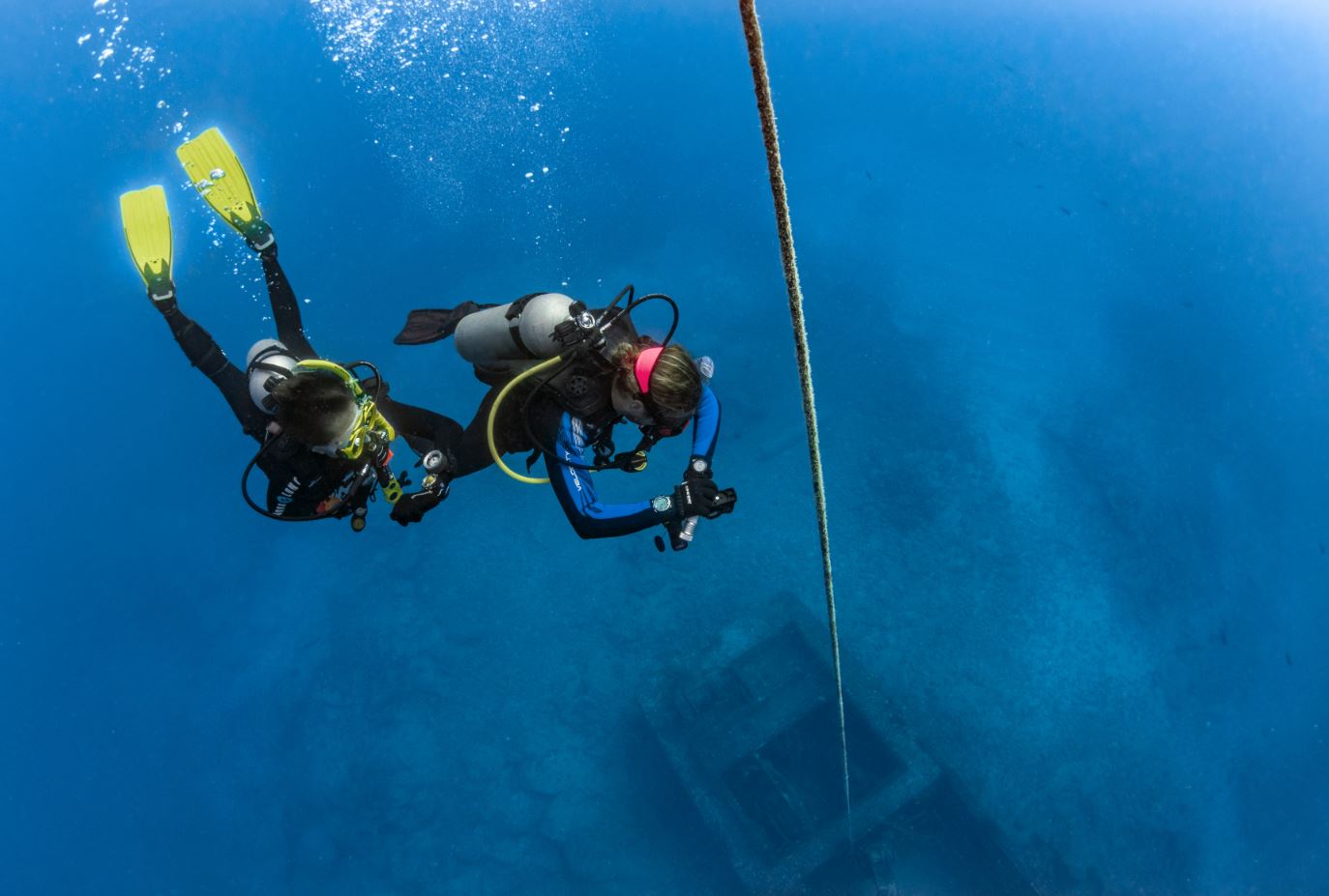 two scuba divers descend towards the bottom of the ocean following a line