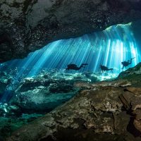 Three divers in Cenote Ponderosa (aka Jardin del Eden) pass across a sunbeam