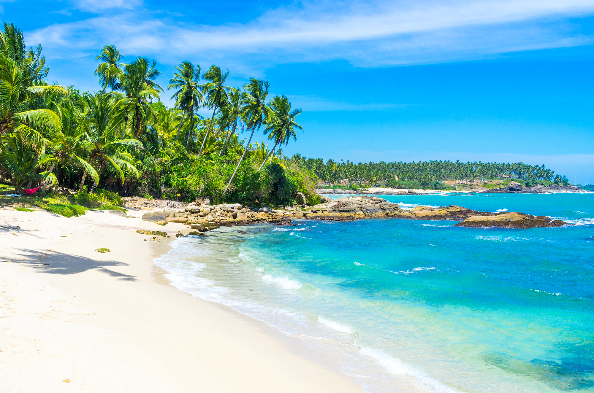 A beautiful white sandy beach with azure waters and palm trees in Sri Lanka, which is a popular scuba diving destination