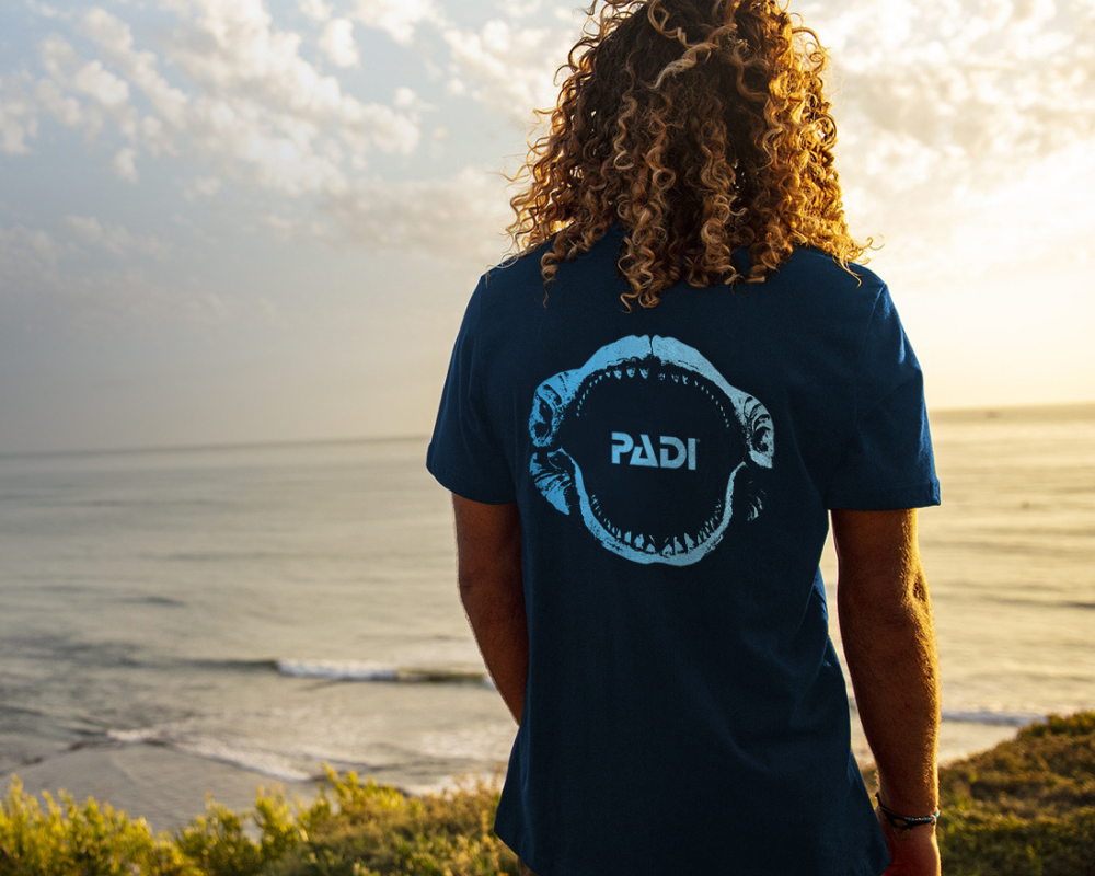 A man looks away from the camera. He is wearing a megladon tshirt from PADI Gear.