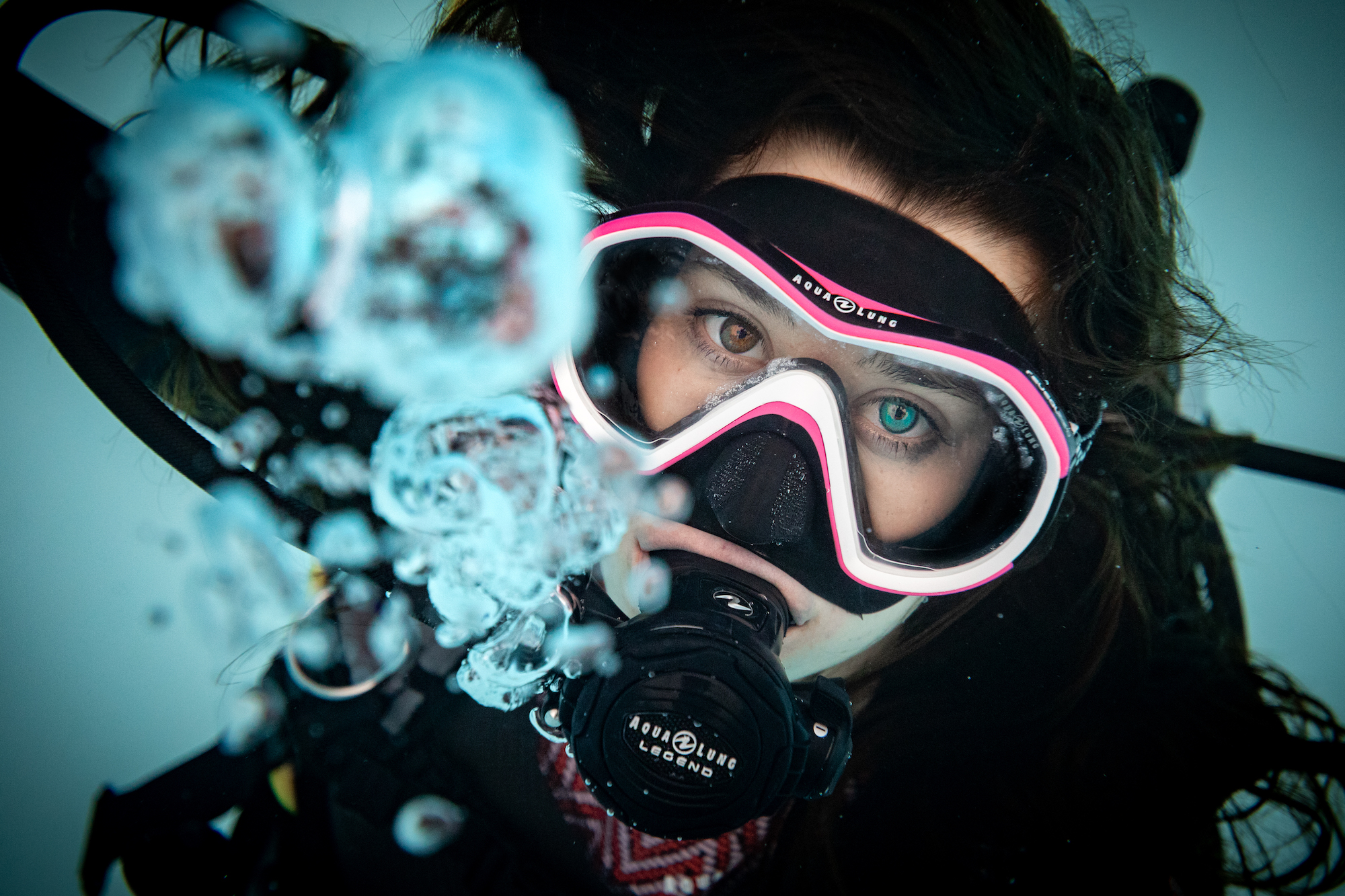A diver in a pink mask clearing their airway and exhaling bubbles through their regulator after coughing or sneezing