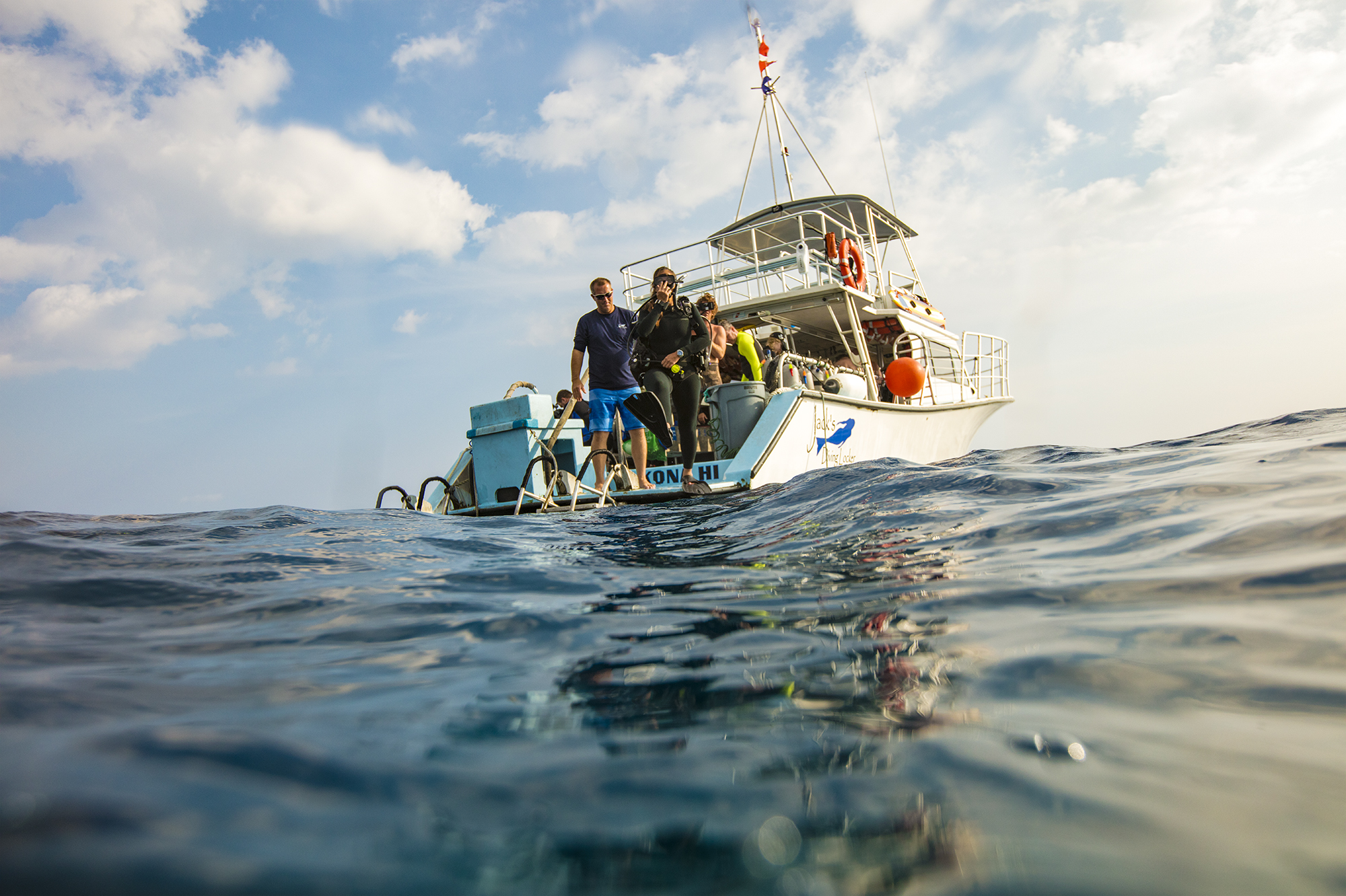 A group of scuba divers jumping into the water from a dive boat under the guidance of a PADI Divemaster