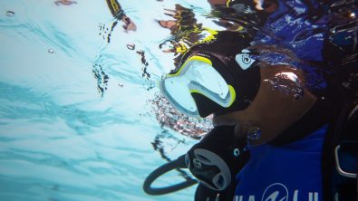 A diver looks underwater with a regulator in his mouth