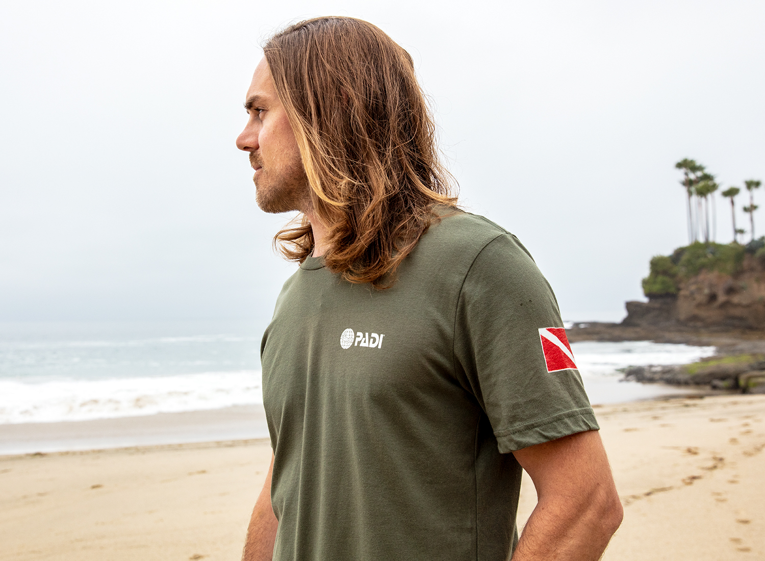 A diver on the beach wearing a t-shirt from PADI Gear which sells eco-friendly school supplies, office gear and scuba fashion