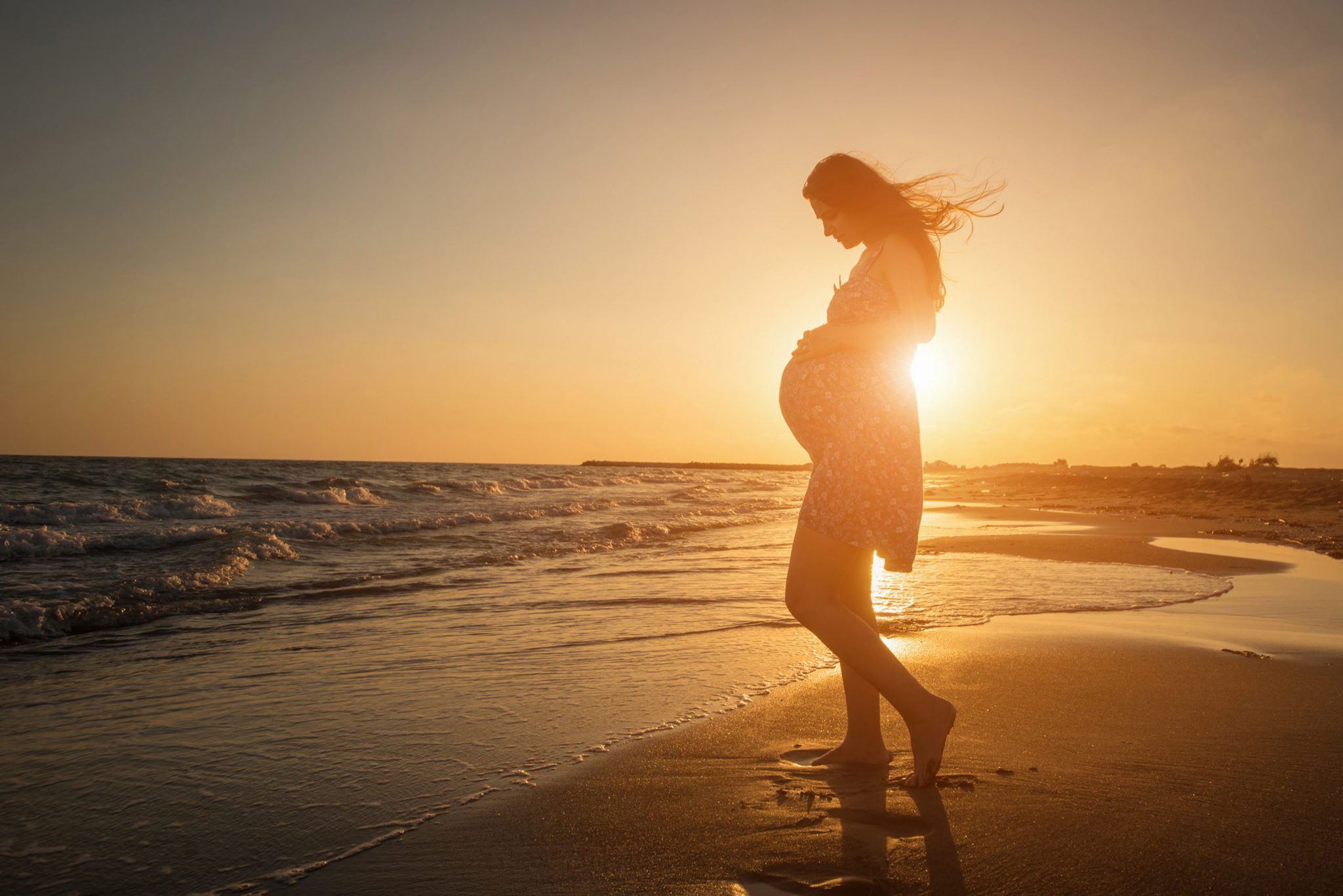 A pregnant woman on a beach at sunset, following the advice to not scuba dive during pregnancy