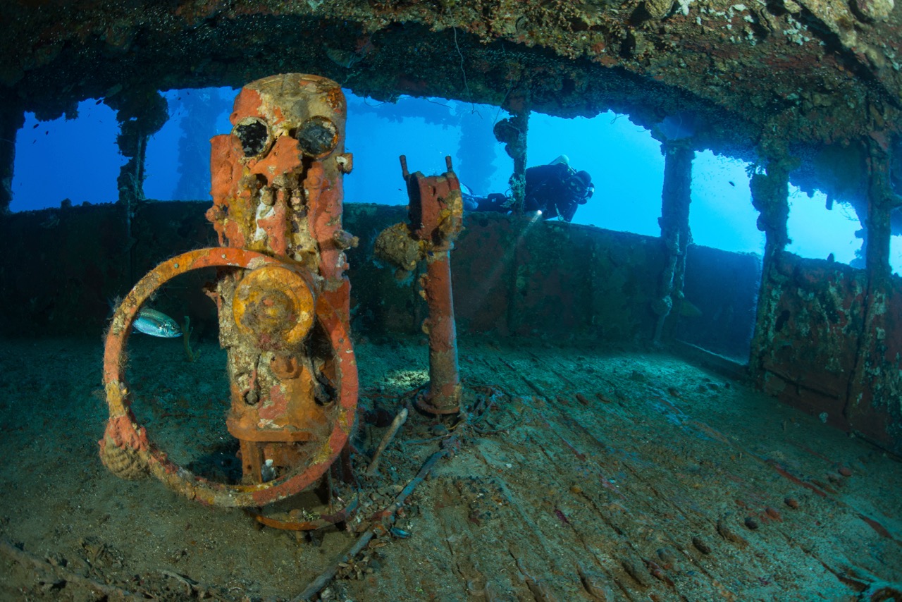 A diver peering into a shipwreck at Truk Lagoon, which is where to go scuba diving in March for some of the best WWII wrecks