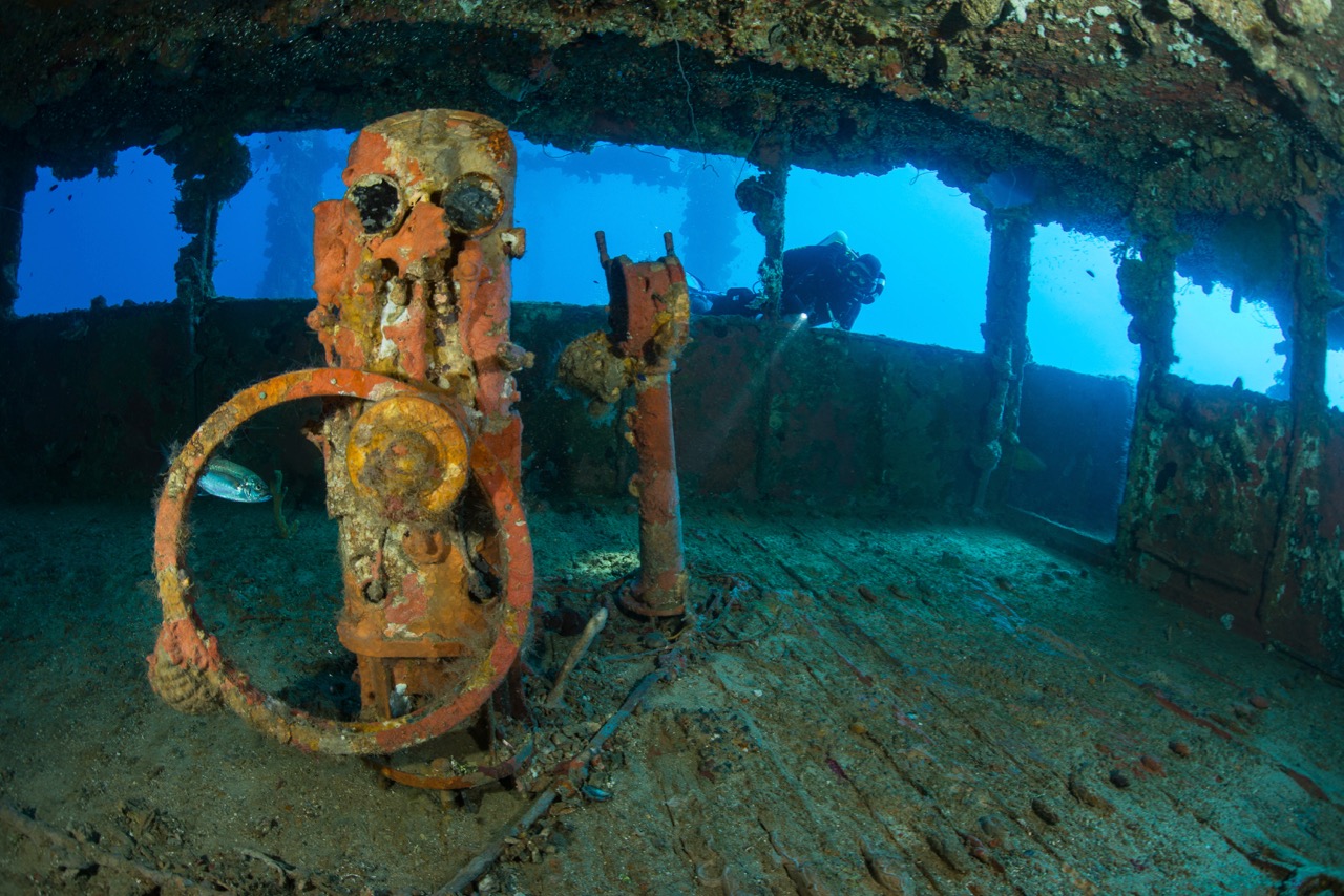 A diver peering into a rusty shipwreck in Truk Lagoon in Southeast Asia, one of the best diving destinations in December