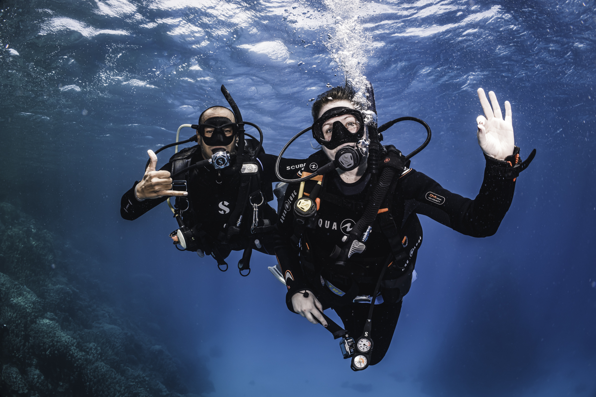 Two divers underwater in Egypt pose for the camera, waving and smiling