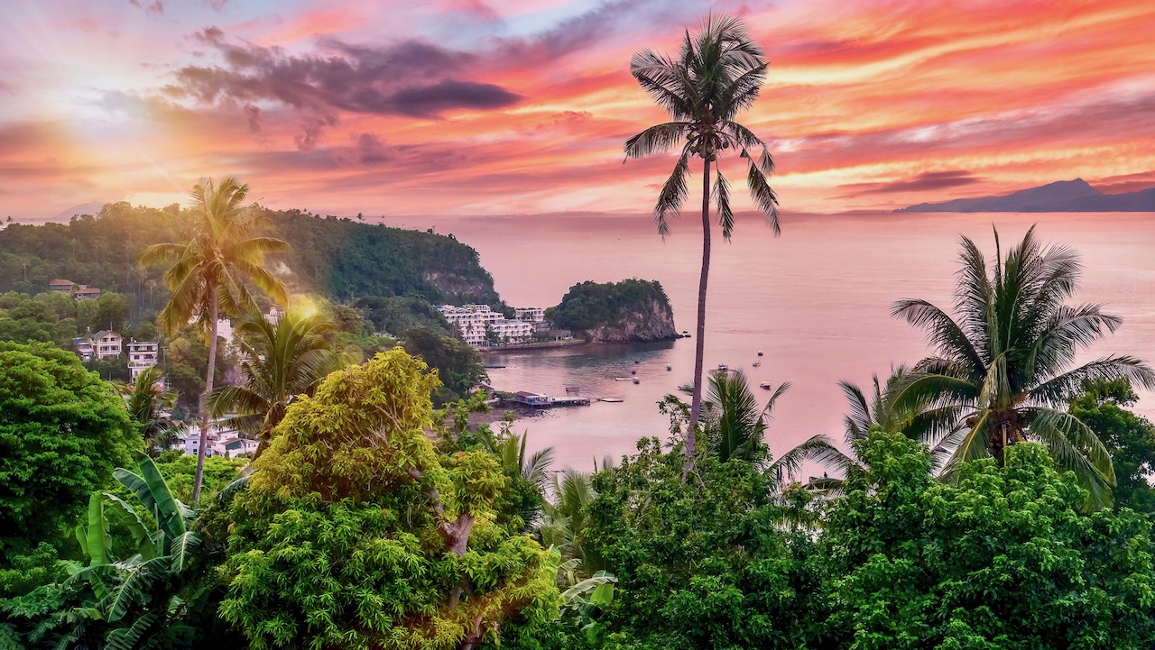 High angle view of the popular dive resort of Sabang Beach in Puerto Galera, Oriental Mindoro, Philippines, with a beautiful pink sunset sky creating an idyllic tropical island scene.