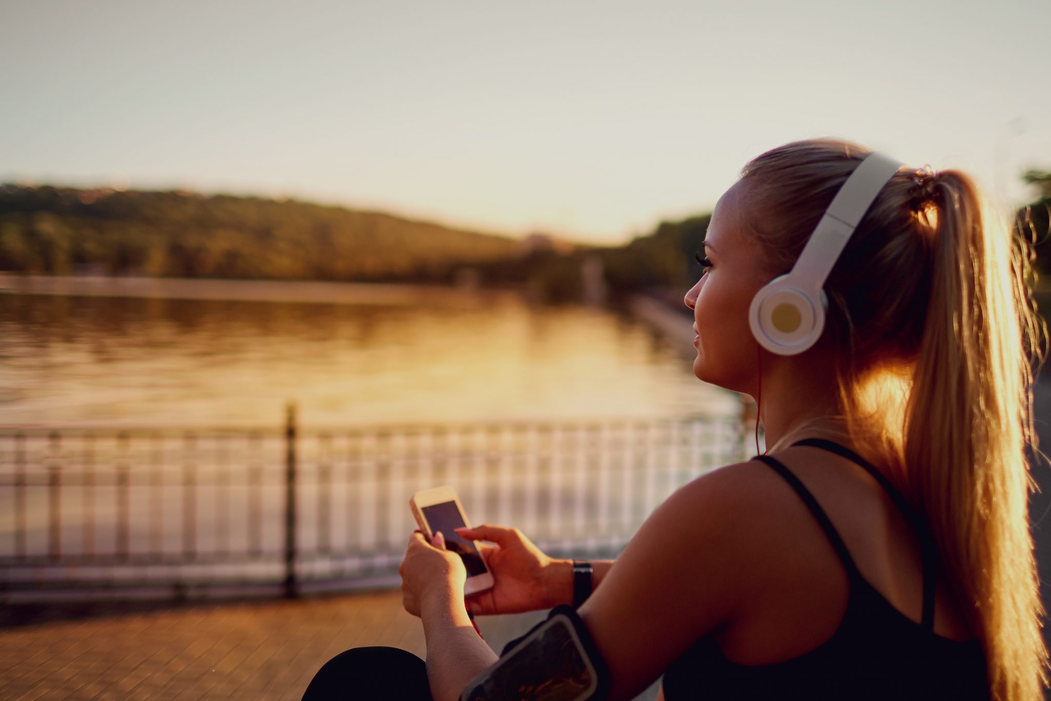 A woman with headphones on rests after exercising near the water