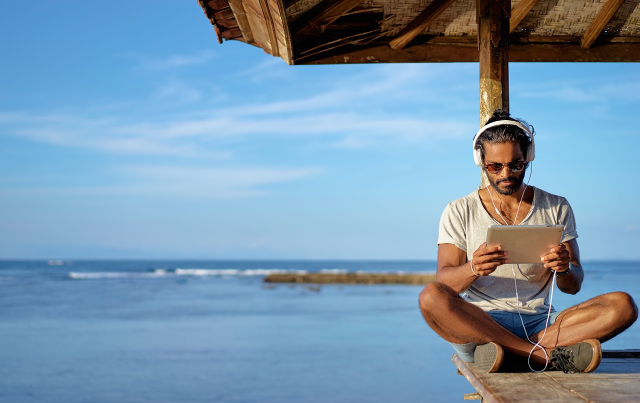 A male scuba diver sits next to the ocean after a day of diving and is relaxing by watching videos from his next PADI course