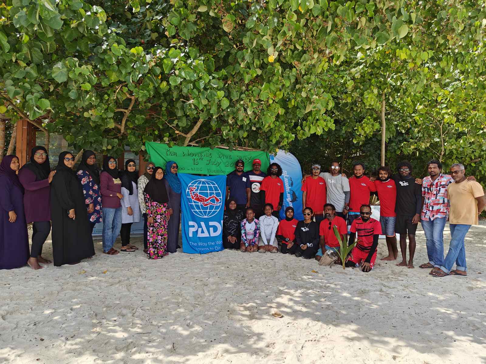 a group of people in the Maldives pose for a photo with a PADI sign