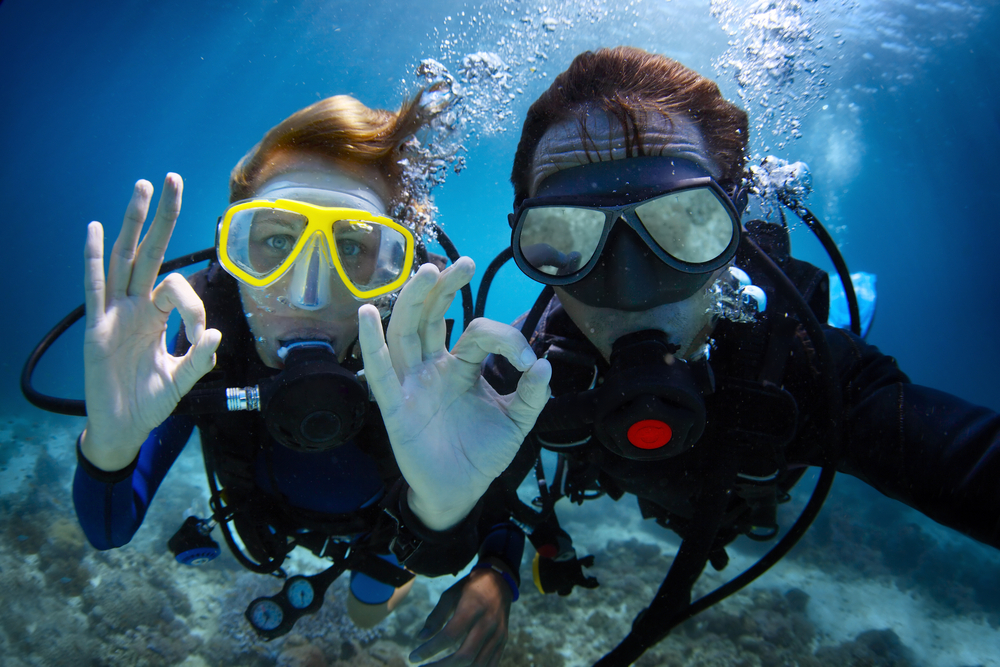 Couple pratiquant la plongée scaphandre et faisant le signe manuel "OK".