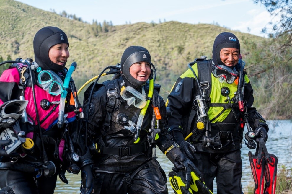 Three Dry Suit Divers getting out of a cold water dive in the mountains.