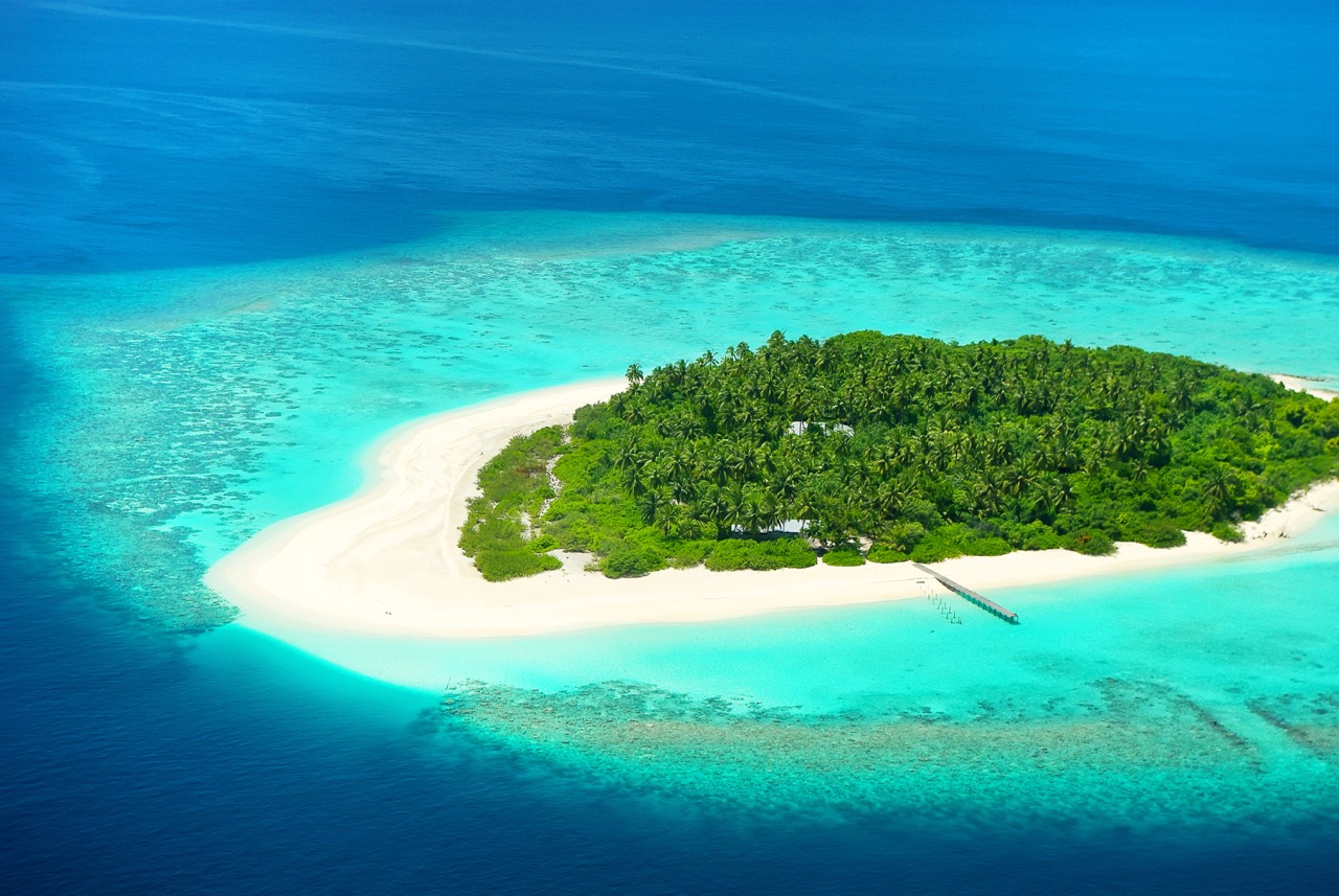 An aerial drone photo of Fuvahmulah Atoll in the Maldives, showing blue ocean, white sandy beaches and lush green vegetation